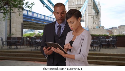 African-American coworkers look over financial data on tablet device in London - Powered by Shutterstock