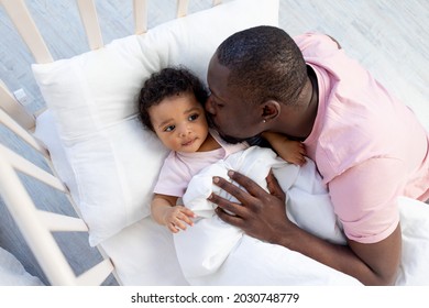 African-American Dad Kisses And Hugs Baby Son In Crib Before Going To Bed