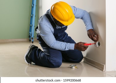 African-American electrician replacing socket in room