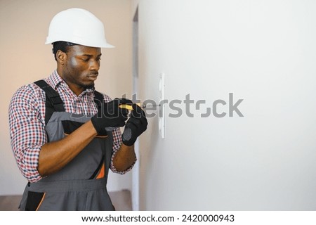 African-American electrician using socket voltage regulator in room.