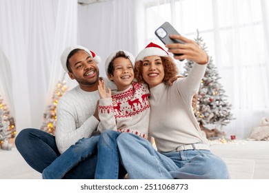 African-American family in Santa hat hugs at home for Christmas and takes selfie near the Christmas tree, teenage boy celebrates the New Year with his mom and dad and takes pictures, parents - Powered by Shutterstock