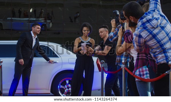 African-American famous
woman walking out of limousine and giving autograph to fan on red
carpet of celebrity
event