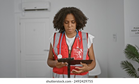 African-american female doctor reviewing notes on tablet in clinic corridor - Powered by Shutterstock