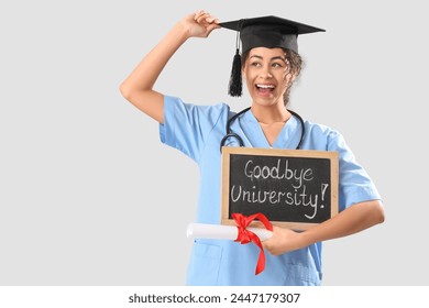 African-American female medical graduate student holding chalkboard with text GOODBYE UNIVERSITY and diploma on white background - Powered by Shutterstock