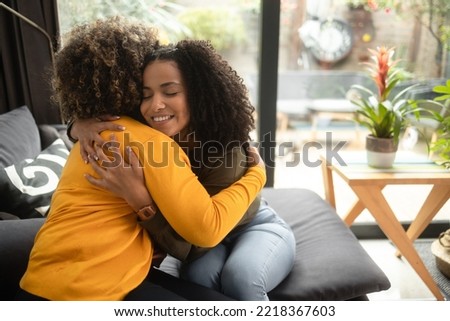 An African-American female psychotherapist comforts the teenage female patient by hugging her. She is smiling because they have made progress. Both of them have the afro hairstyle.
