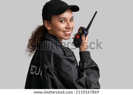 African-American female security guard with radio transmitter on light background