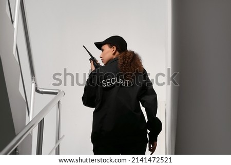 African-American female security guard with radio transmitter in building, back view