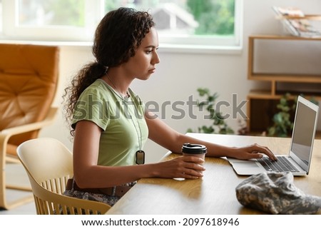 African-American female soldier with laptop drinking coffee at home