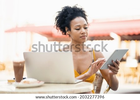 An African-American freelancer working prints a message to a client by mail. A woman is sitting in a summer cafe in the city.