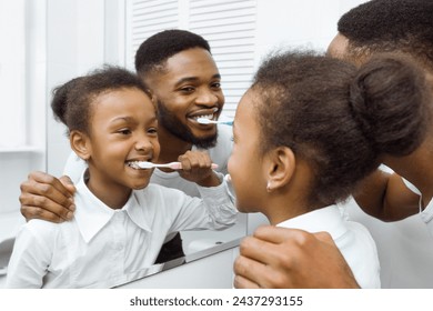 African-american girl brushing teeth with dad in bathroom - Powered by Shutterstock