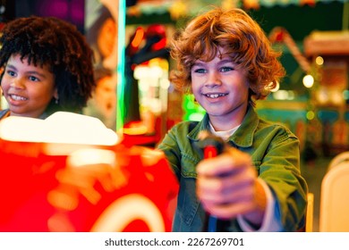 An African-American girl child with an Afro hairstyle and a cute Caucasian boy sitting in an amusement car ride playing a computer game racing in an amusement park.