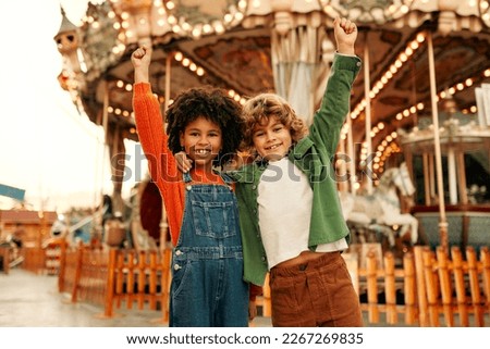 An African-American girl child and a Caucasian boy with a curly hairstyle have fun in an amusement and amusement park.