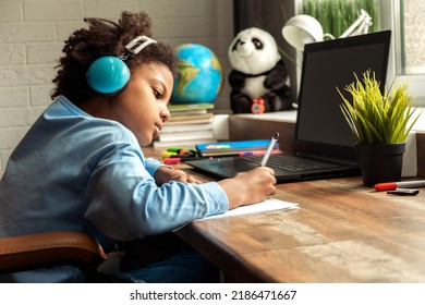 African-American Girl Doing Homework,making Notes,using Headphones And Laptop At Home.Back To School Concept.School Distance Education At Home,home Schooling,e-learning,diverse People.Copy Space.