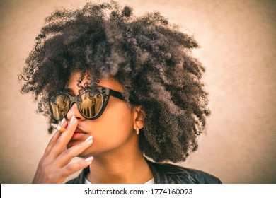 African-American girl with sunglasses smokes a cigarette. She smokes with pleasure. - Powered by Shutterstock