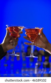 African-American Hands Toast Martini Glasses Against A Bright Blue Background. Vertical Shot.