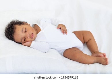 African-American little baby sleeps on a white bed at home with her hand folded under her cheek