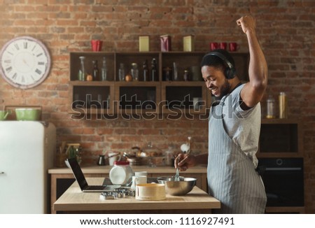 African-american man in earphones listening to music and dancing while baking in kitchen