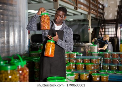 African-American man engaged in producing of pickled olives, controlling quality of products in cans - Powered by Shutterstock