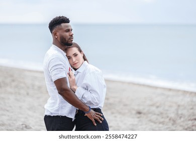 An African-American man and a Latina woman embrace tenderly by the shore at Zapillo Beach. The tranquil ocean waves gently lap at the sandy beach as they share a quiet moment together - Powered by Shutterstock