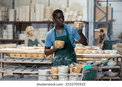 African-american man potter evaluating quality of new crafted ceramic bowls in workshop. - Powered by Shutterstock