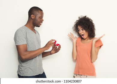 African-american man proposing to his shocked and surprised girlfriend at white isolated studio background. Wedding, romance, love, family and valentine day concept, copy space