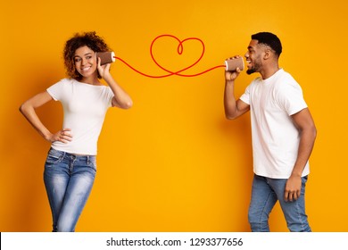 African-american man singing love song to his girlfriend via tin phone, orange studio background, copy space