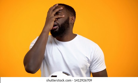 African-American Man With Soccer Ball Watching Match, Showing Face Palm Sign