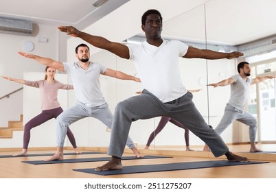 African-american man standing in warrior two pose during group yoga training in gym. - Powered by Shutterstock