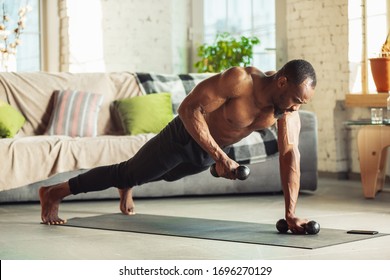 African-american man teaching at home online courses of fitness, aerobic, sporty lifestyle while being quarantine. Getting active while isolated, wellness, movement concept. Training with weights.