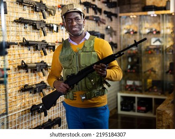 African-american Man Wearing Armor And Helmet While Standing With Assault Rifle In Airsoft Shop.