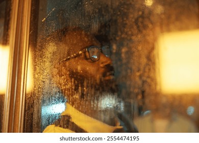 An African-American man wearing eyeglasses leaning against a rainy bus window as seen from outside with his eyes closed. - Powered by Shutterstock