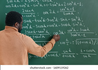 African-American Math Teacher Writing On Blackboard In Classroom