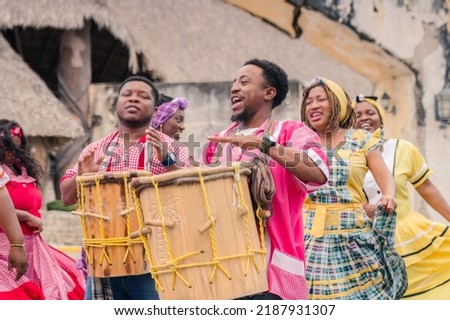 African-American men play drums and women dance to their Caribbean music in the park.