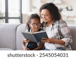 African-american mother mom reading fairy tales book novel with daughter girl, learning together, helping assisting with homework for school. Female tutor teaches schoolgirl at home. Homeschooling