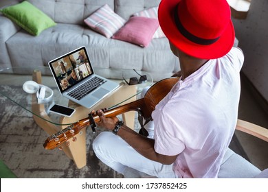 African-american musician playing guitar during online concert at home isolated and quarantined. Using camera, laptop, streaming, recording courses. Concept of art, support, music, hobby, education. - Powered by Shutterstock