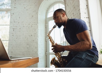 African-american musician playing saxophone during online concert at home isolated and quarantined. Using camera, laptop, streaming, recording courses. Concept of art, support, music, hobby, education - Powered by Shutterstock