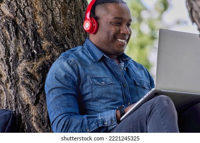 An African-American Popular Musician Is Engaged In The Processing Of Electronic Music In Headphones In A City Park. A Black Music Producer Listens To Music And Takes Notes On A Laptop