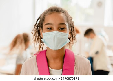 African-american schoolgirl kid pupil student wearing protective face mask against Covid19 coronavirus at lesson in school during pandemic. - Powered by Shutterstock