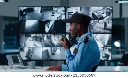 African-American security officer watching the screens talking on radio in control room 