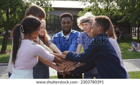African-American teacher and teen students put hands together and hug outside school. Portrait of happy professor and college students embrace outdoors