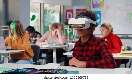 African-American teen student sit down and desk and put on vr headset. Schoolboy study in virtual reality goggles in classroom - Powered by Shutterstock