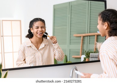 African-American Teenage Girl Brushing Teeth Near Mirror In Bathroom