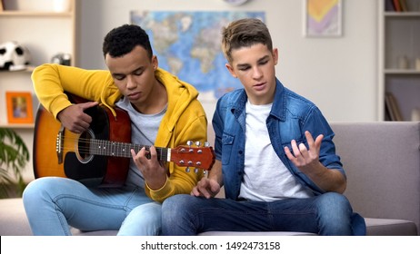 African-American teenager teaching Caucasian friend to play guitar, hobby - Powered by Shutterstock