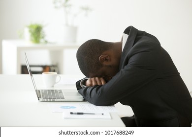 African-american tired deprived businessman feeling lack of sleep having nap at workplace, black restless entrepreneur hopeless by bankruptcy or debt, depressed investor desperate about failure