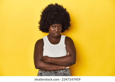 African-American woman with afro, studio yellow background frowning face in displeasure, keeps arms folded. - Shutterstock ID 2347147459