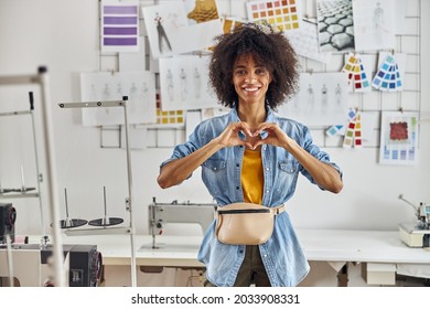 African-American Woman Designer Shows Heart With Hands Near Sewing Machine In Workshop