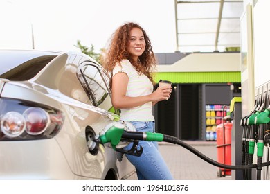 African-American woman drinking coffee while filling up car tank at gas station