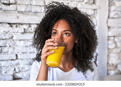 African-American woman enjoys freshly squeezed orange juice on sofa, morning light. - Powered by Shutterstock