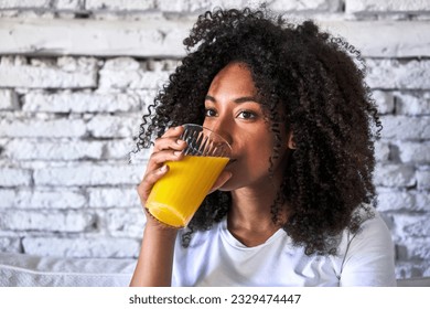 African-American woman enjoys freshly squeezed orange juice on sofa, morning light. - Powered by Shutterstock