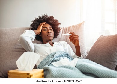 African-American woman feeling sick at home. Lying in bed, drinking tea and medicine. Sick woman checking the result of thermometer. Cold And Flu. Portrait Of Ill African American Woman Caught Cold - Powered by Shutterstock